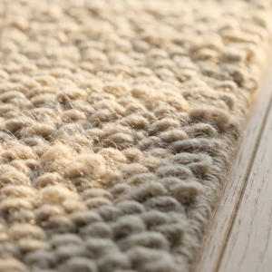 D&eacute;tail macro d'un tapis en laine ivoire pos&eacute; sur un parquet ch&ecirc;ne clair, lumi&egrave;re rasante lat&eacute;rale du matin qui met en &eacute;vidence la texture du velours et l'effet mat chaleureux de la fibre